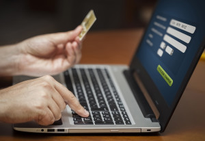 Hombre frente al ordenador con una tarjeta de crédito efectuando una compra online.